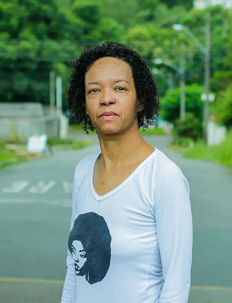 Silvanna Bárbara, professora do Escola Nota 10, com uma blusa de manga longa branca e cabelo cacheado curto